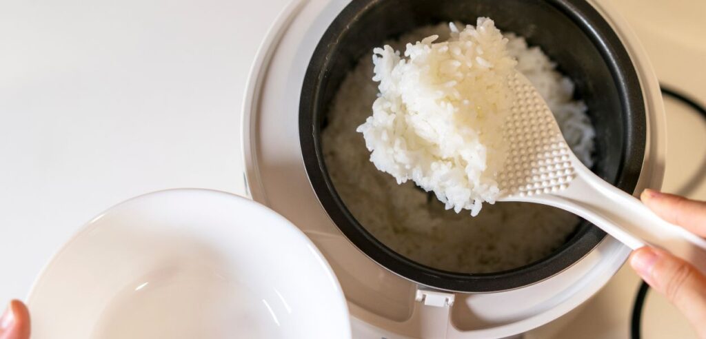 person serving cooked white rice out of a white rice cooker