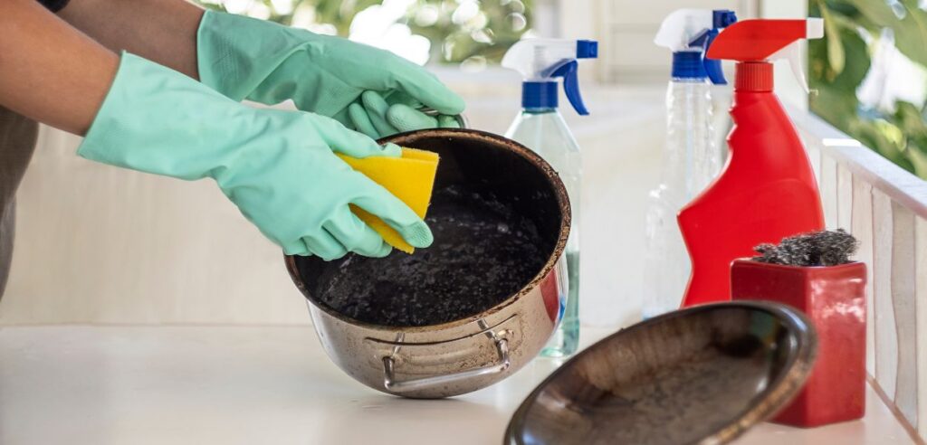 person cleaning a dirty pot with rice burned in it